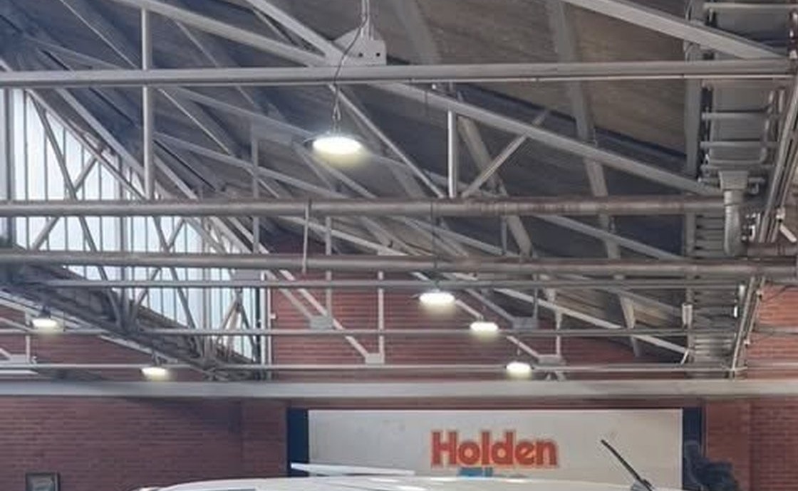 Steel truss roof and brick walls inside the Forbes Automotive Services workshop, with the old Holden dealership sign still mounted on the back wall